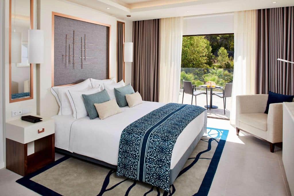 Quarto do Tivoli Carvoeiro com cama de casal do lado esquerdo da imagem, com uma cômoda do lado direito da cama e em frente a cama uma poltrona do lado  esquerdo da cama. Representa hotéis 5 estrelas em Portugal.