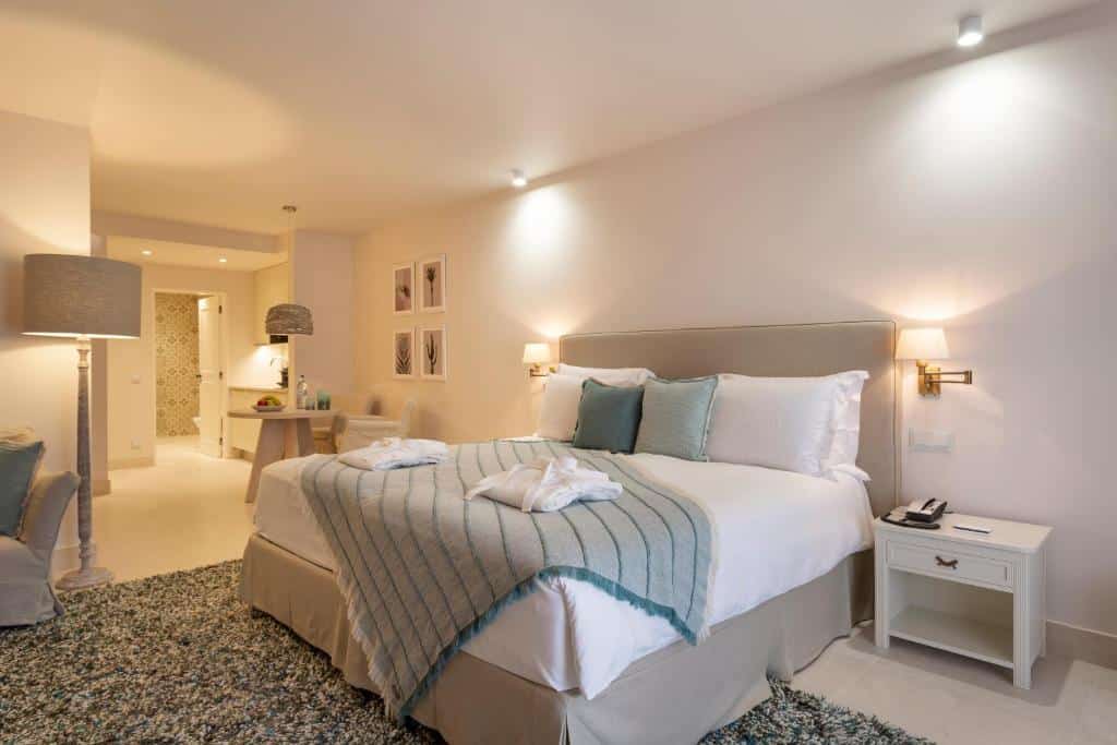 Quarto do Vila Vita Parc Resort & Spa com cama de casal do lado direito da imagem, com uma cômoda do lado direito da cama e do lado esquerdo uma mesa redonda com duas cadeiras. Representa hotéis 5 estrelas em Portugal.