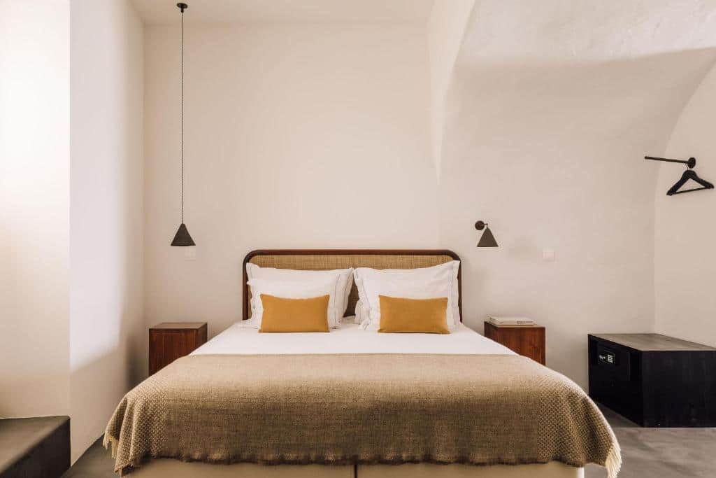 Quarto do White Exclusive Suites & Villas com cama de casal no centro do quarto com uma cômoda de madeira em cada lado da cama e do lado direito da cama um cofre encostado na parede. Representa hotéis 5 estrelas em Portugal.