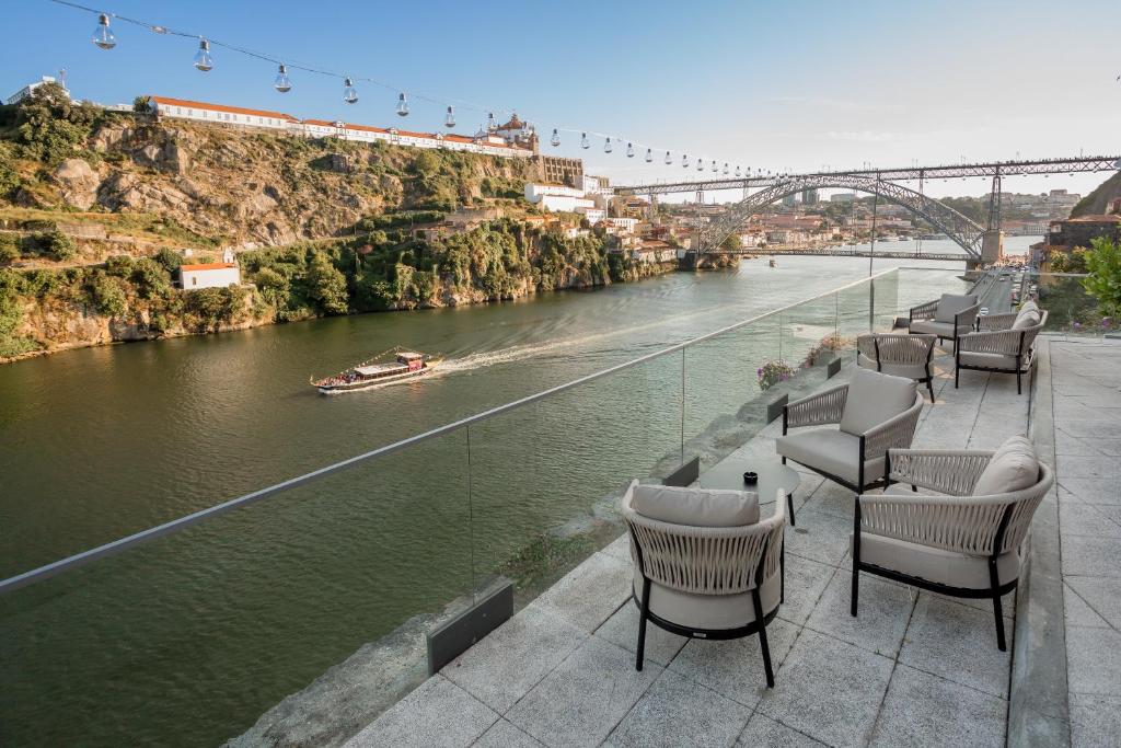 Sacada do Eurostars Porto Douro durante o dia com varanda do lado direito da imagem com cadeiras do lado esquerdo o rio Douro com um barco navegando sobre as águas.
