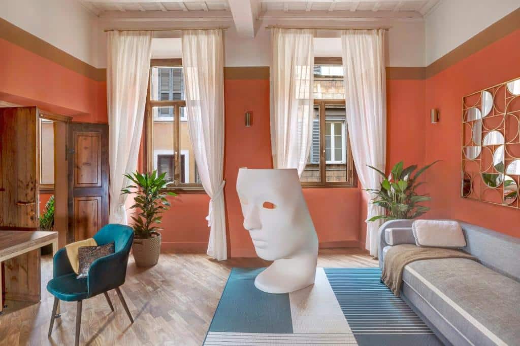 sala do Luxury Trevi House, com tapete no chão, sofá branco e duas janelas de madeira com cortinas claras, há mesa com cadeira de madeira e uma escultura que representa uma máscara