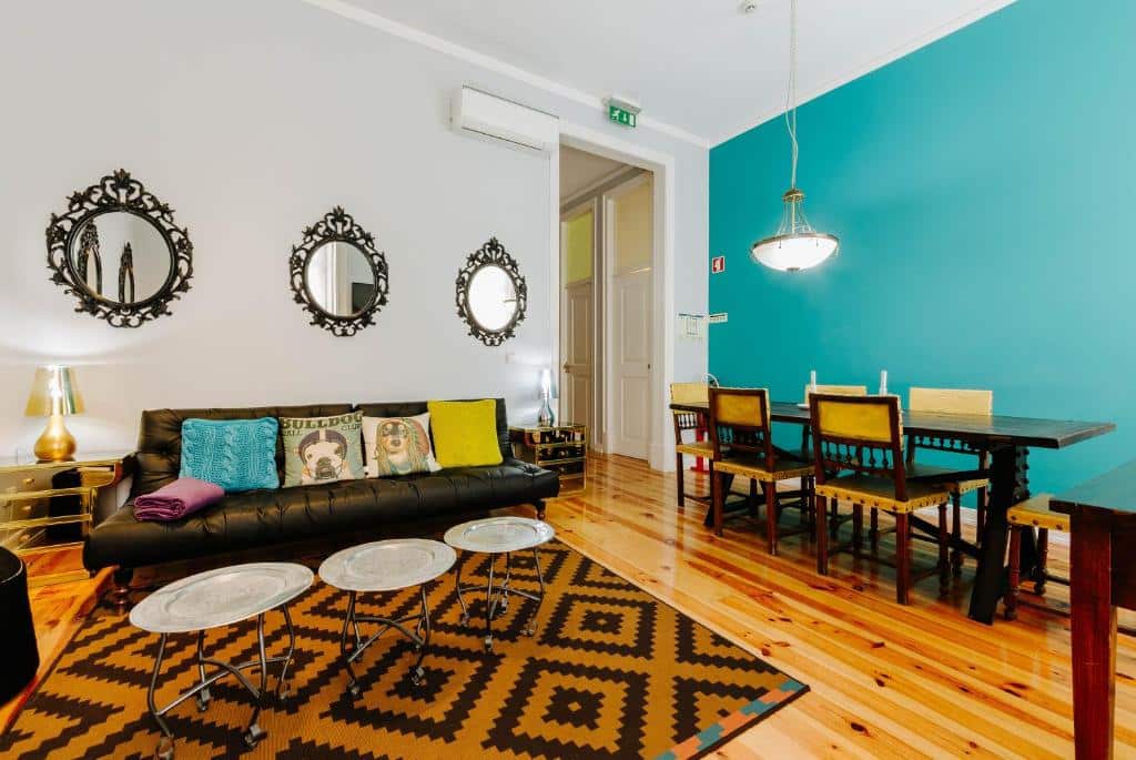 Sala de estar e de jantar integradas em uma dos apartamentos do Lisbon Art Stay Apartments Baixa, do lado direito há uma mesa de madeira com seis lugares, do lado esquerdo está um sofá com almofadas, uma mesinha de centro e alguns espelhos redondos na parede