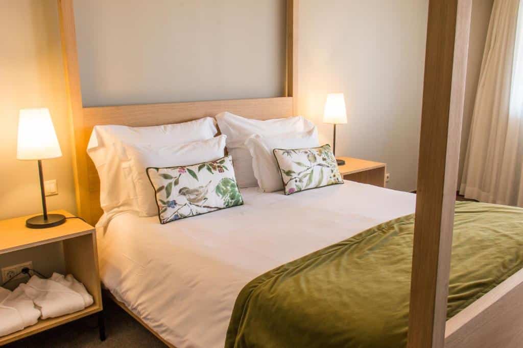 Quarto do Evora Hotel. A cama de casal possui quatro travesseiros, duas almofadas e em cada lado da cama há mesinhas com abajures. Imagem para ilustrar o post hotéis no Alentejo.