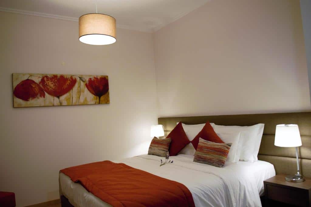 Quarto do hotel Vistas - Herdade do Zambujal. A cama está encostada na parede do lado direito e há em cada lado da cama uma pequena mesa com abajur. Imagem para ilustrar o post hotéis no Alentejo.