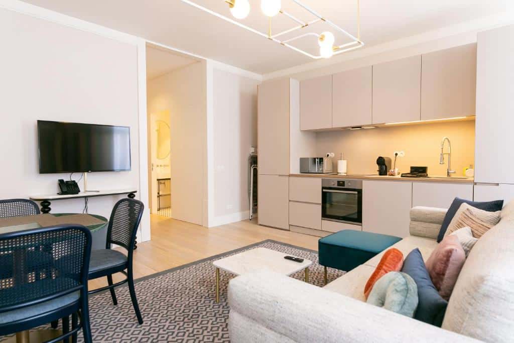 Sala de estar do The Lift Apartments by RIDAN Hotels integrado com uma mini cozinha com forno e utensílios gerais, ao lado está um sofá com almofadas e de frente para ele há uma televisão e uma mesa redonda com quatro cadeiras