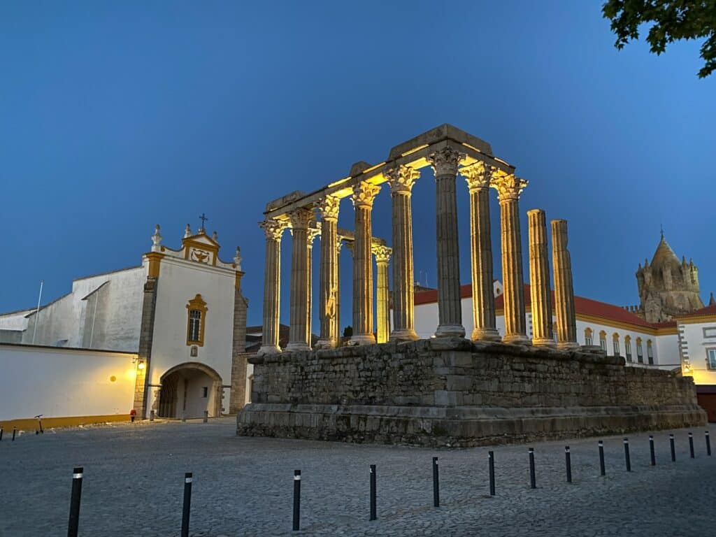 Uma estrutura antiga com formato de arquitetura grega com diversas colunas gregas em frente de uma igreja antiga em Évora