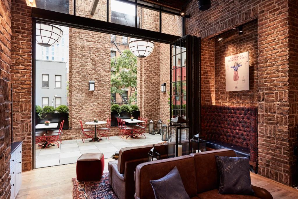 lounge compartilhado do CIVILIAN Hotel com sofás de couro marrom, paredes de tijolos expostos e uma área aberta no terraço com mesas brancas e cadeiras de metal vermelhas.
