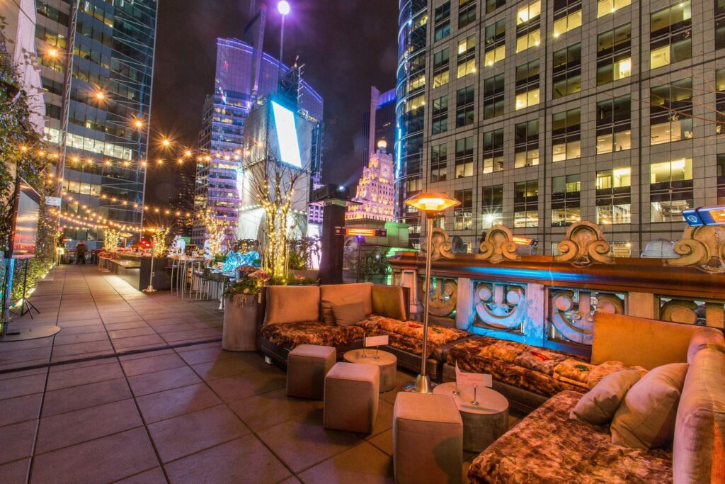terraço do The Knickerbocker com várias luzinhas espalhadas pelo espaço, além de diversos pufes, sofás e bancos altos. O espaço é todo decorado com iluminação e tem vista para a bola de ano novo da Times Square.