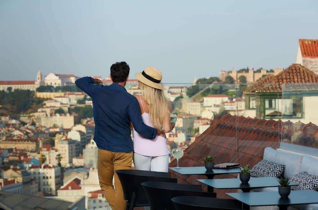 Terraço do The Lumiares Hotel & Spa - Small Luxury Hotels Of The World com vista para a cidade, no local há mesas e cadeiras, e há um casal próximo do vidro que protege o local observando a vista, para representar hotéis para brasileiros em Lisboa