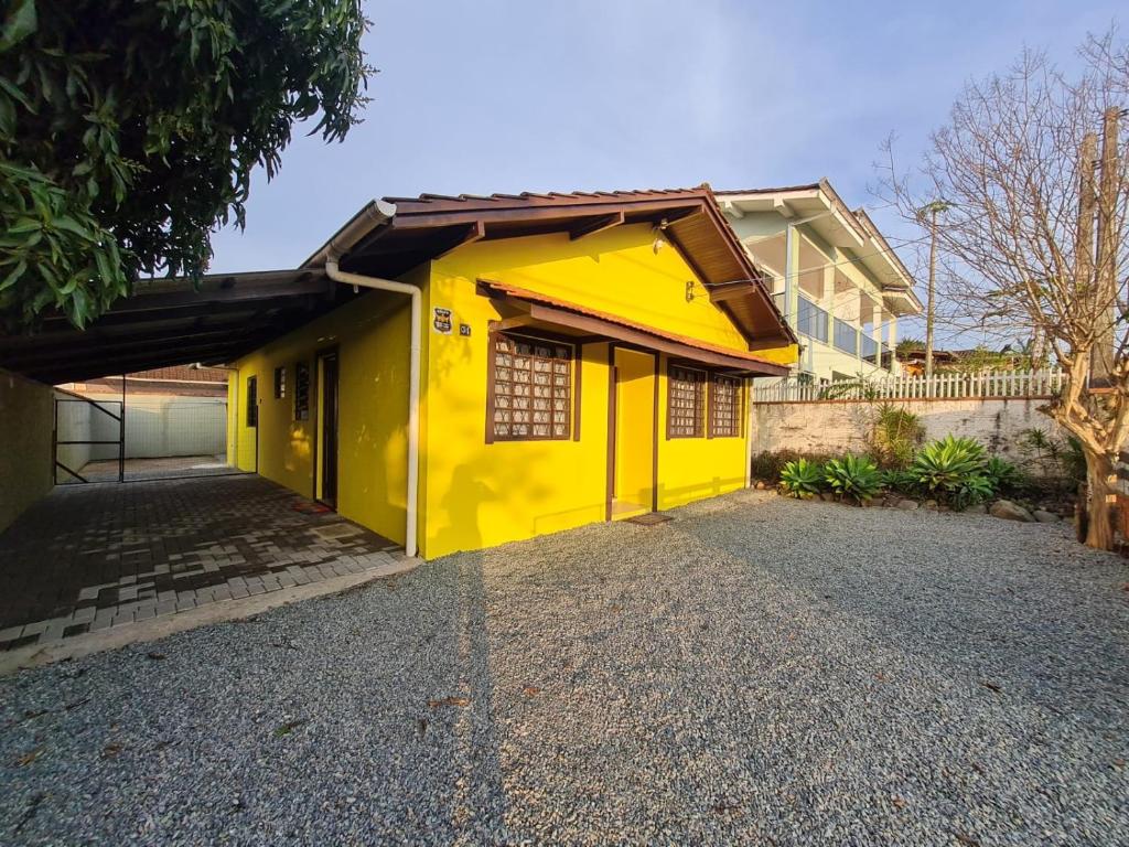Casa de aluguel The Yellow House mostrando uma casa amarela com um quintal de pedrinhas grande e espaçoso. Há também uma varanda coberta no lado esquerdo da casa.