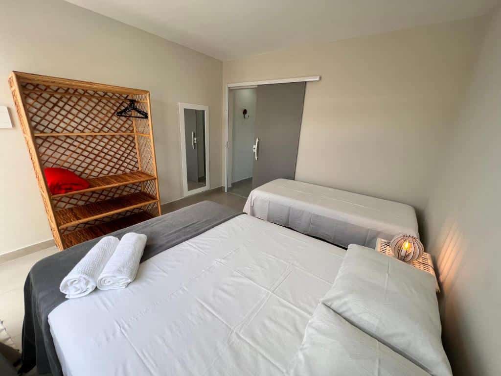Quarto da VilaMar Jacuípe em Camaçari. Uma cama de casal uma cômoda com abajur e uma cama de solteiro no lado direito. De frente um guarda-roupa e um espelho, no fundo a porta do quarto.