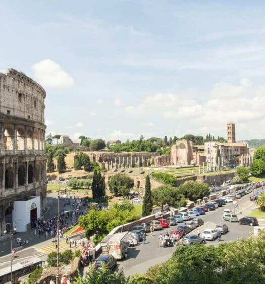 vista do B&B Colosseo Panoramic Rooms, uma das opções de onde ficar em Roma, que dá direto para o Coliseu, há apenas uma rua separando o espaço, e tem vários carros, mais ao longe é possível ver o Fórum Romano
