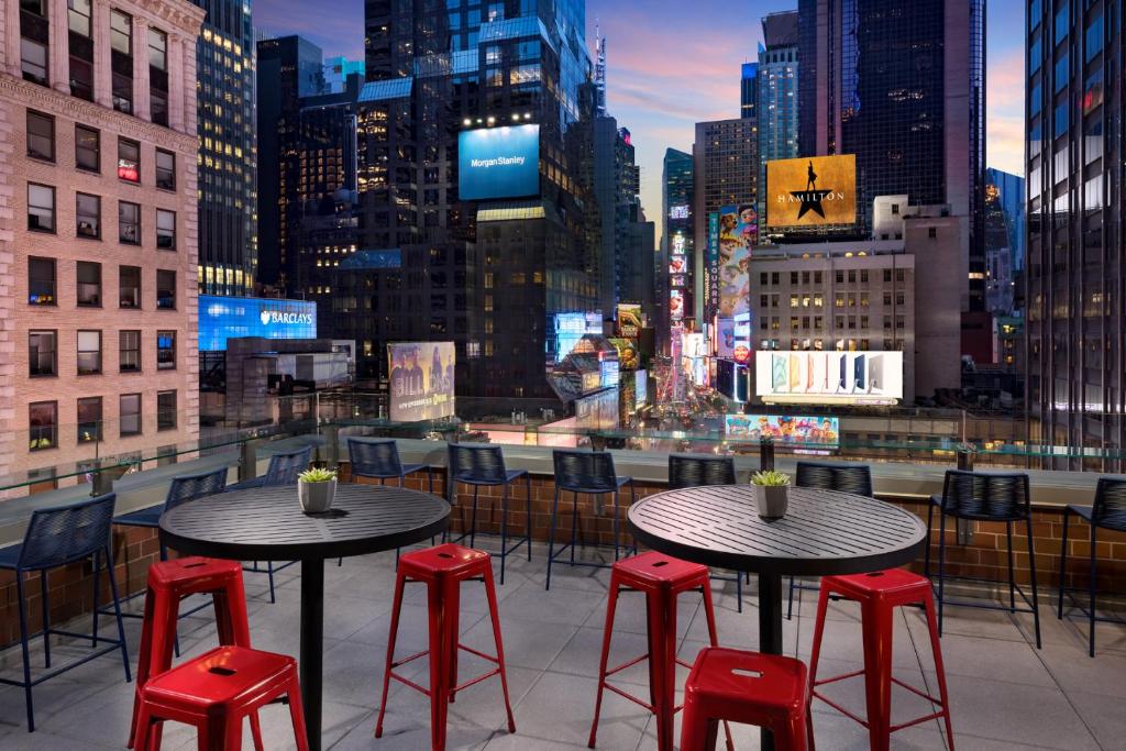 terraço do M Social Hotel Times Square New York com vista para os prédios e outdoors da Times Square. Há várias cadeiras e mesas para se sentar e jantar.