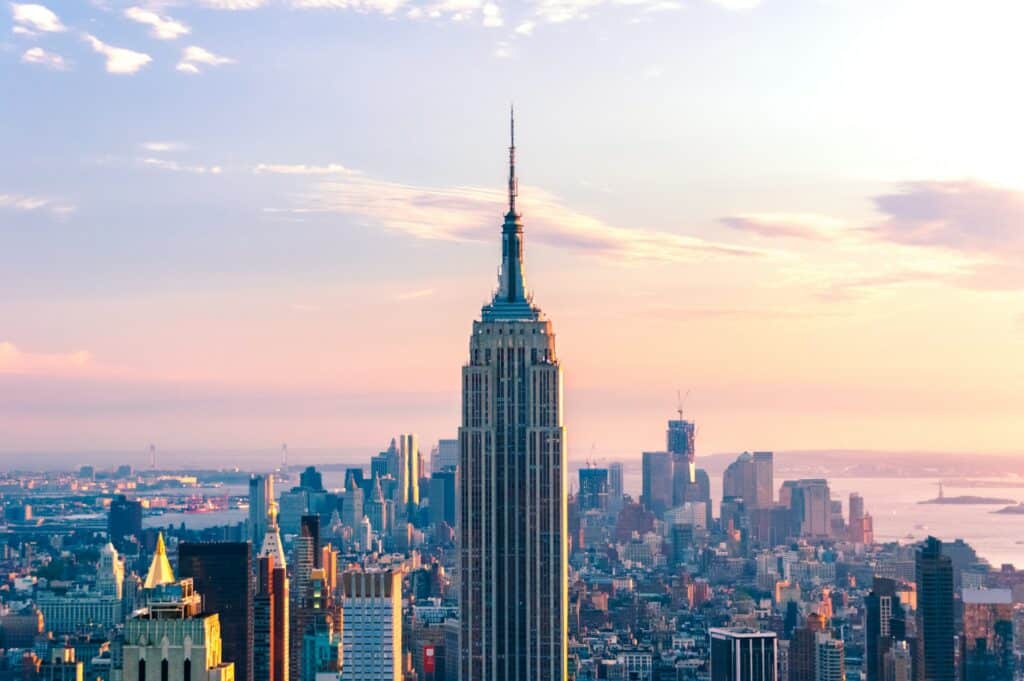 vista do Empire State Building, uma das opções de o que fazer em Nova York, com sua torre imponente e bastante pontuda, ao redor de outros prédios mais baixos à tarde