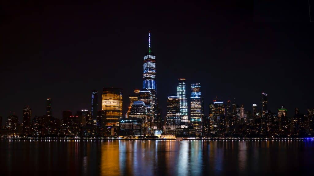 vista à noite do Wall St., Financial District, em Nova York, com prédios luminosos com seus reflexos na água