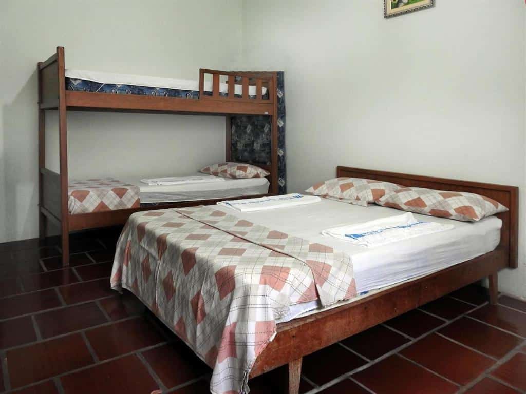 Quarto da Associação Sabesp Ilha Comprida. Uma cama de casal na frente, atrás uma cama de beliche. Foto para ilustrar post sobre pousadas em Ilha Comprida.