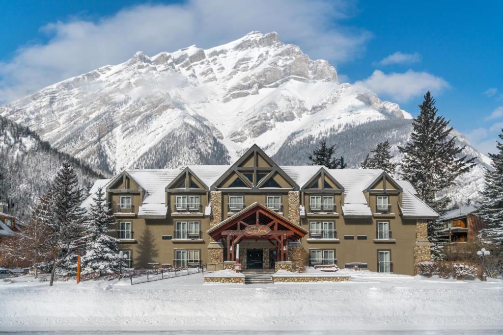 Fachada do hotel Banff Inn na cor marrom com três andares e telhados pontudos. Em volta tem algumas árvores cobertas por neve e ao fundo uma montanha coberta por neve também, ilustrando post Hotéis em Banff.