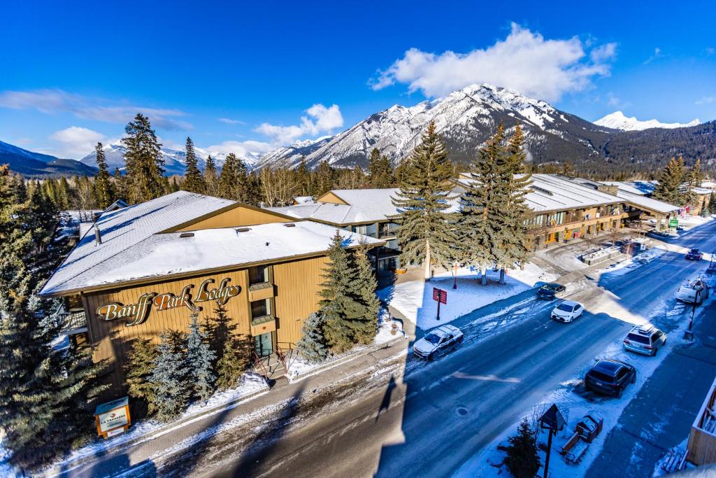 Fachada do Banff Park Lodge na cor amarelo com o letreiro na parede e telhado coberto por neve. Em volta tem algumas árvores, carros parados na rua e ao fundo uma montanha coberta por neve, ilustrando post Hotéis em Banff.