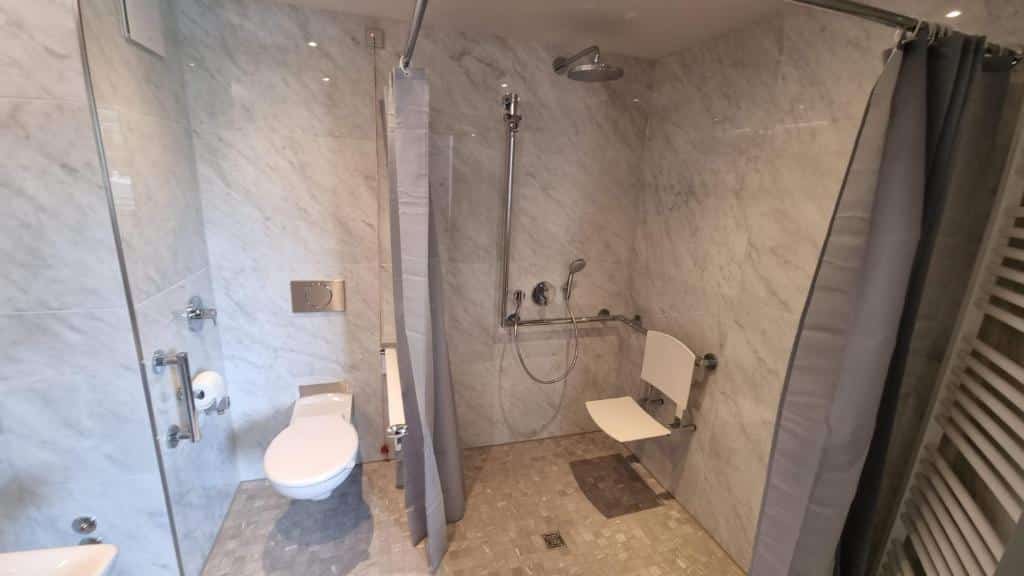 Banheiro com acessibilidade do Fourty Three Luxury Serviced Apartments do lado direito da imagem chuveiro com barras de apoio e do lado esquerdo vaso sanitário com barra de apoio.