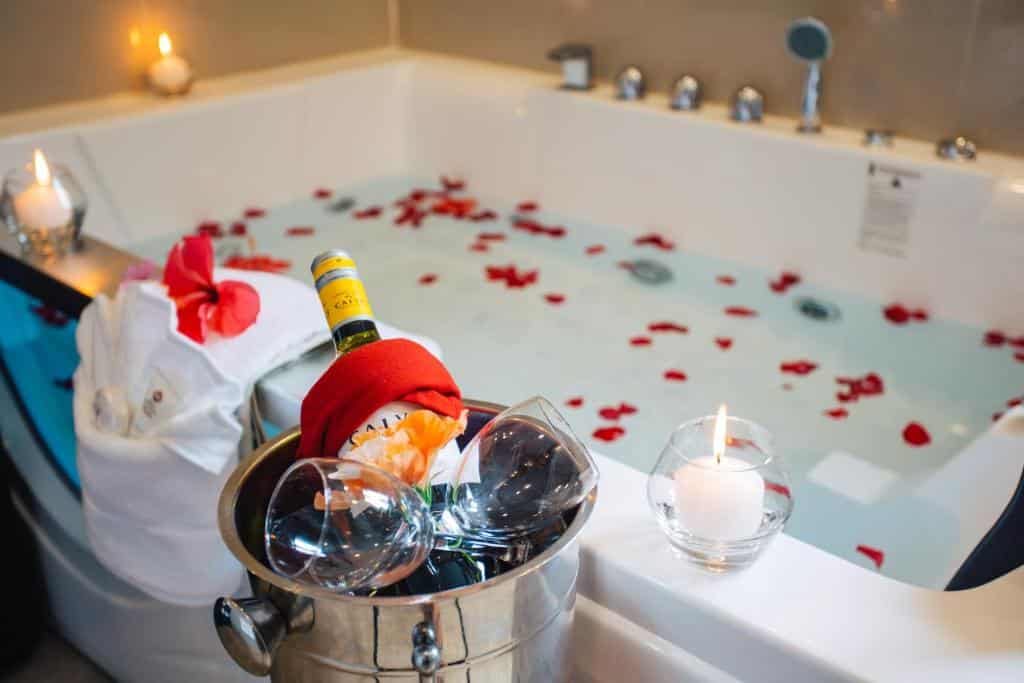 Foto da hidro no Best Western Plus Belize. A hidro está com pétalas de rosa dentro. O foco da câmera vai para o balde de champagne na beirada da hidro, também há algumas velas.