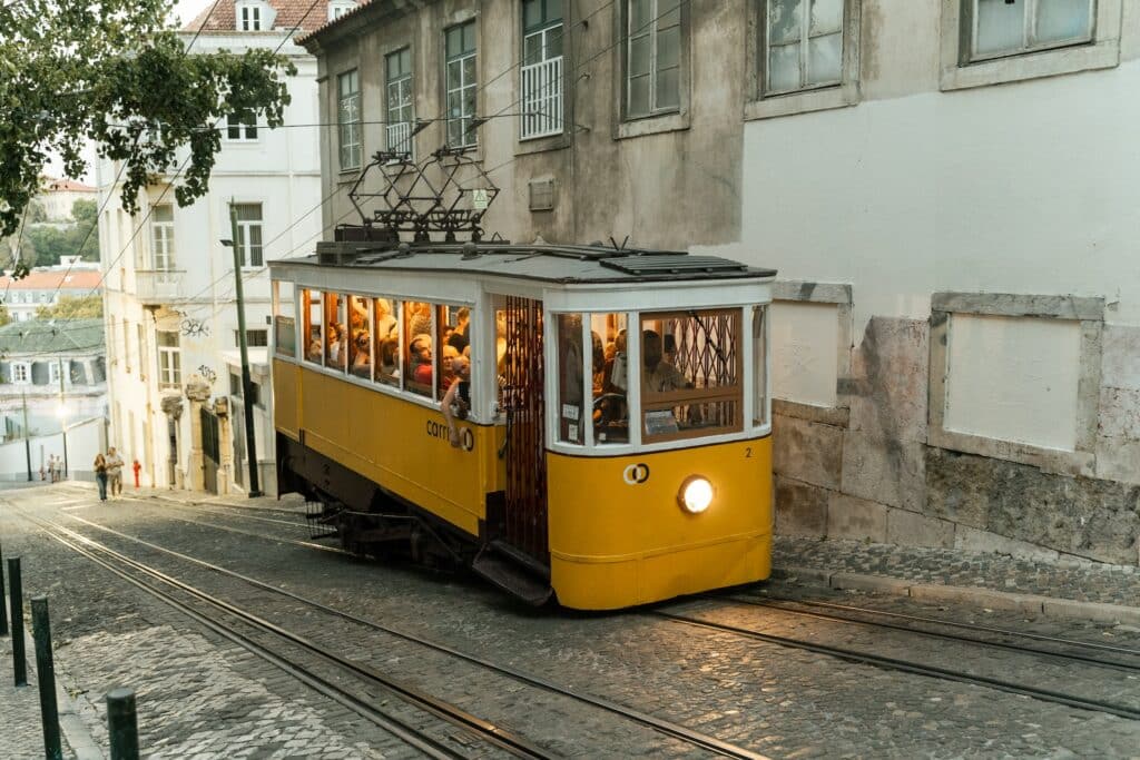 Bondinho amarelo, cheio de pessoas, subindo ladeira de Lisboa, um dos destinos mais visitados da Europa