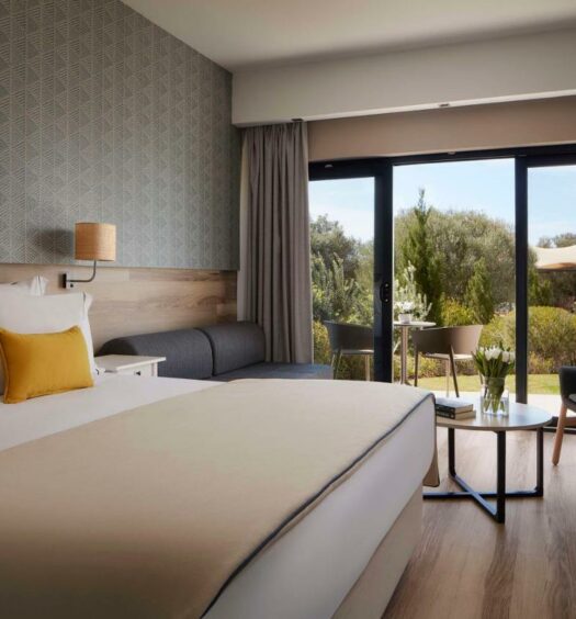 Quarto do Tivoli Alvor Algarve - All Inclusive Resort,com cama de casal do lado esquerdo da imagem, do lado esquerdo da cama um sofá com mesa de centro e do lado esquerdo do sofá uma porta de vidro com acesso a varanda. Representa hotéis all inclusive em Portugal.