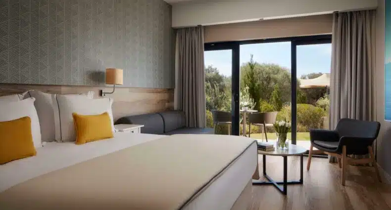 Quarto do Tivoli Alvor Algarve - All Inclusive Resort,com cama de casal do lado esquerdo da imagem, do lado esquerdo da cama um sofá com mesa de centro e do lado esquerdo do sofá uma porta de vidro com acesso a varanda. Representa hotéis all inclusive em Portugal.