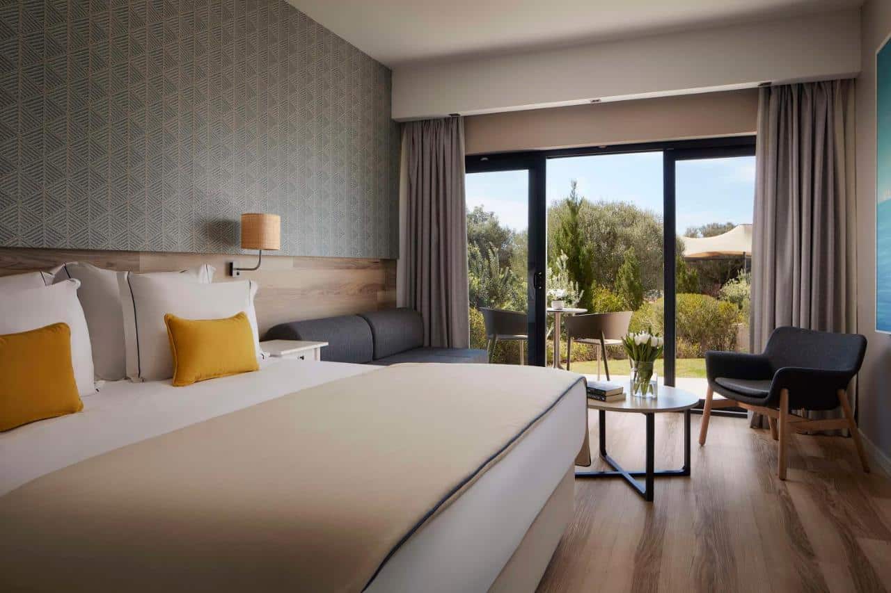 Quarto do Tivoli Alvor Algarve - All Inclusive Resort,com cama de casal do lado esquerdo da imagem, do lado esquerdo da cama um sofá com mesa de centro e do lado esquerdo do sofá uma porta de vidro com acesso a varanda. Representa hotéis all inclusive em Portugal.
