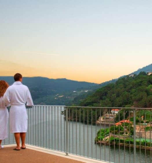 Casal parado na varanda no Douro Royal Valley Hotel & Spa, durante o dia olhando o rio Douro. Representa hotéis para lua de mel em Portugal.