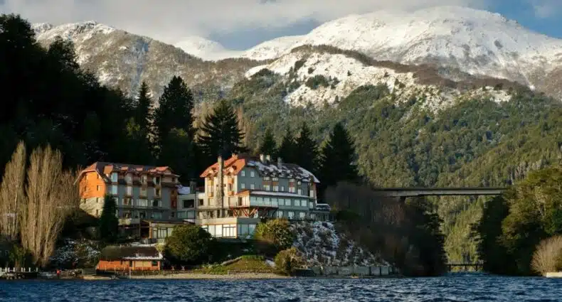 O prédio do hotel Correntoso Lake & River Hotel no canto esquerdo. Atrás as montanhas, e na frente e ao redor o lago. Foto para ilustrar post sobre hotéis em Villa La Angostura.