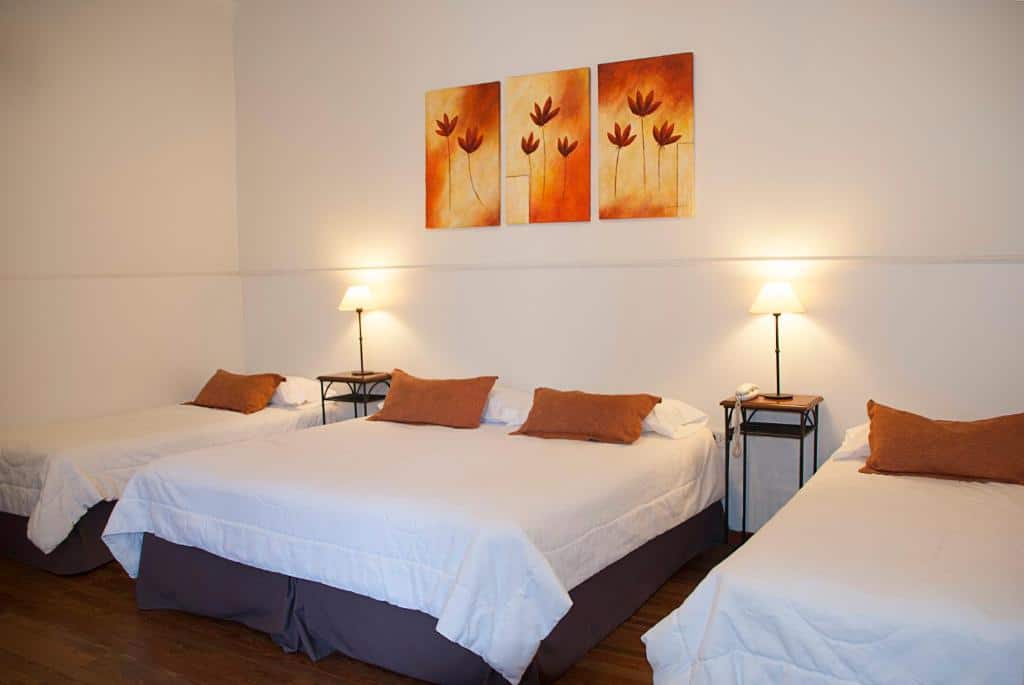 Quarto do El Arribo Hotel. Uma cama de casal no meio e uma cama de solteiro de cada lado. Entre as camas uma mesinha com um abajur. Foto para ilustrar post sobre hotéis em Jujuy.