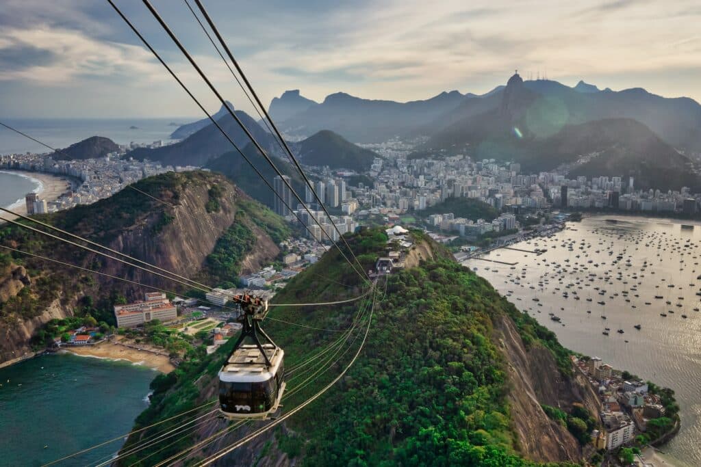 Um bondinho descendo em direção de uma montanha alta onde é possível ver o mar e os prédios na cidade do Rio de Janeiro