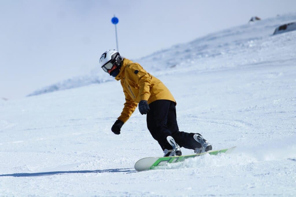 Um homem usando calça preta e jaqueta amarela em cima de uma prancha de esqui em um local com muita neve, para representar seguro viagem Argentina