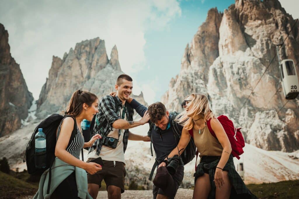 Um grupo de amigos, com duas mulheres e dois homens, se abrançando e rindo em frente de algumas montanhas, para representar seguro viagem internacional