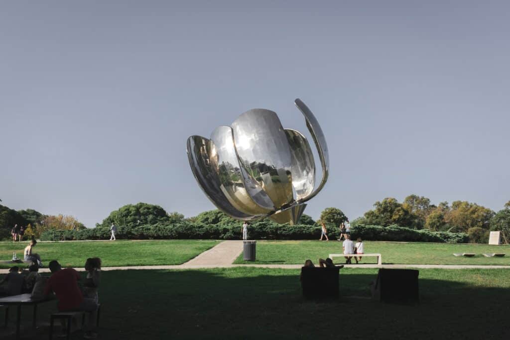 Floralis generica, em Buenos Aires. O objeto é uma esculta grande de metal no formato de uma flor, localizada em um campo gramado com alguns bancos e pessoas sentadas em volta