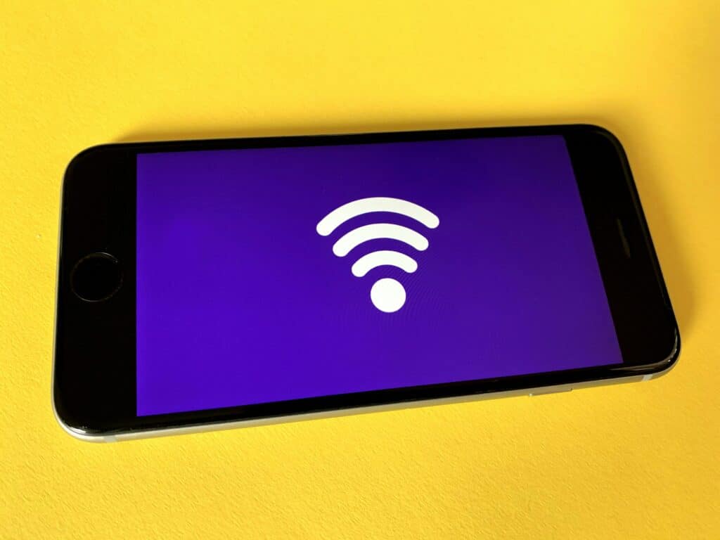 Celular em cima de uma mesa amarela com uma tela roxa aparecendo com um desenho do sinal de wi-fi