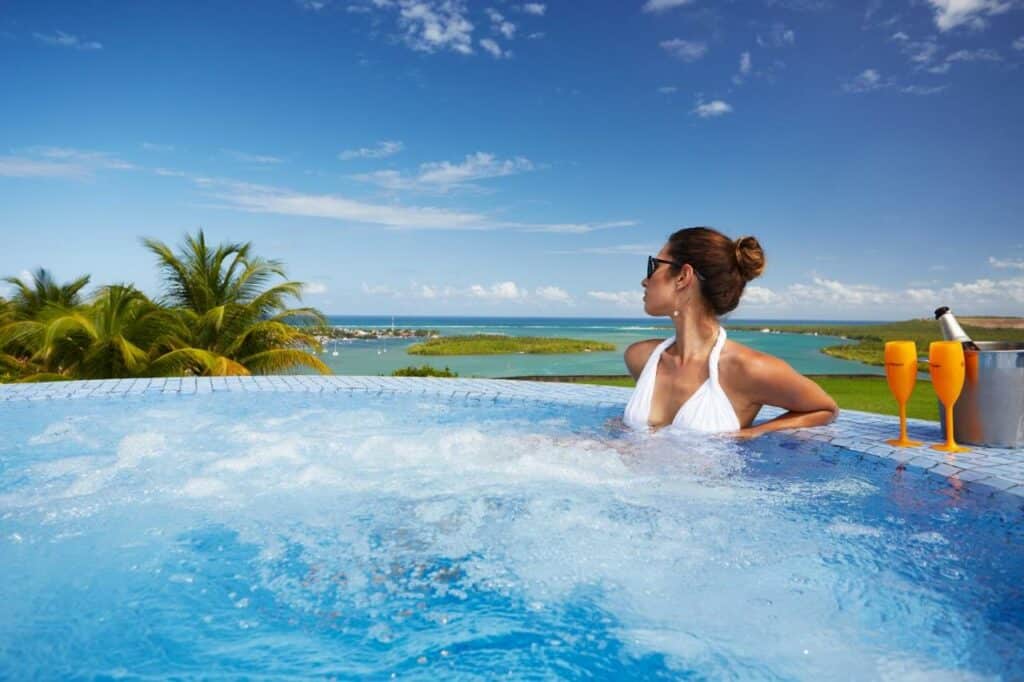 Mulher dentro de uma hidro no Gungaporanga Hotel com coque no cabelo e usando óculos de sol olhando para o lado. Há uma paisagem atrás do mar e árvores