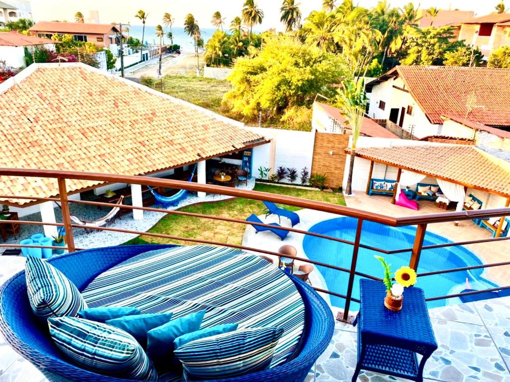 Parte do Hotel e Pousada Cumbuco Guesthouse que mostra um sofá redondo azul com algumas almofadas e uma mesinha com uma flor encostados na grade da varanda e embaixo está a piscina e alguns lugares cobertos com redes e cadeiras para as pessoas, ilustrando post Hotéis em Cumbuco.