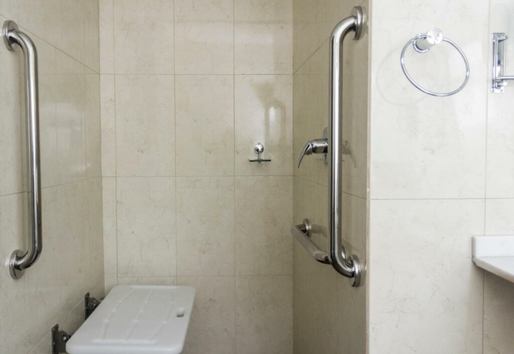 Área de banheiro adaptado no Hotel Vinocap, com assento para banho e barras de apoio no chuveiro
