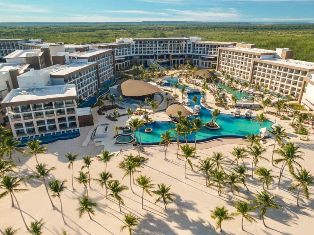 Vista aérea do Hyatt Ziva Cap Cana, que tem uma grande piscina rodeada por palmeiras e com os prédios do resort ao redor. Uma faixa de areia com mais palmeiras está no lado inferior.