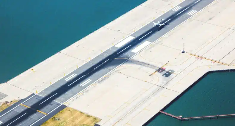 vista aérea da pista de pouso do Aeroporto LaGuardia em Nova York. Há uma única aeronave pousando na pista. Ao lado da pista é possível ver o mar margeando o espaço.