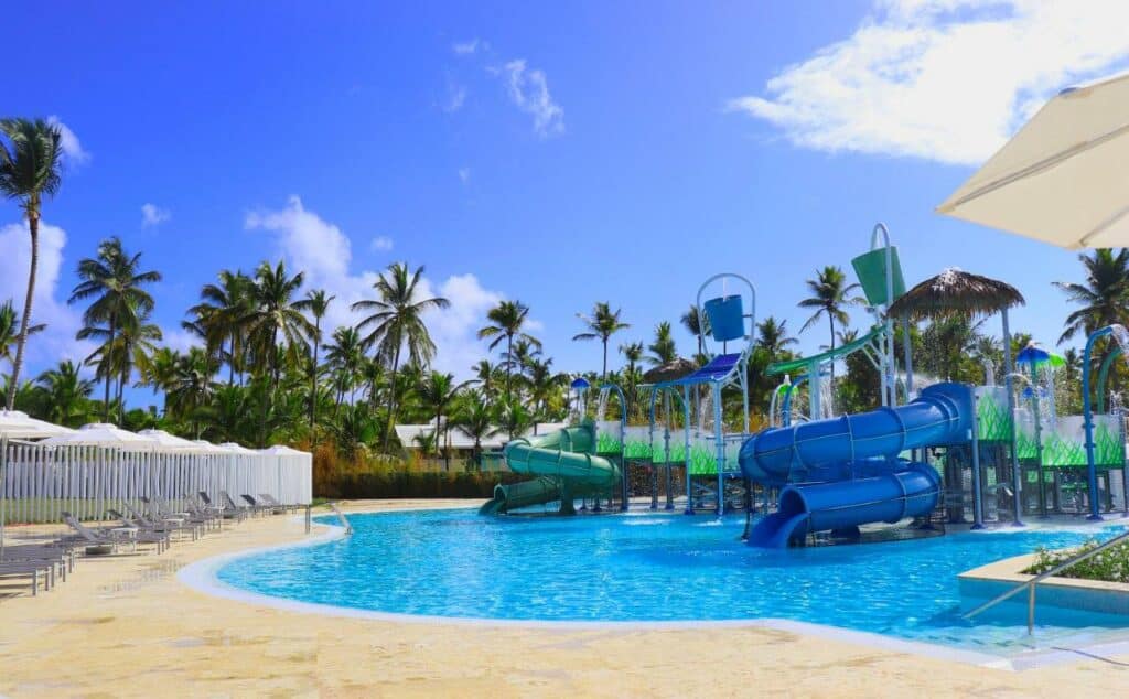 Parque aquático do Meliá Caribe Beach. Vários tobogãs e estruturas aquáticas estão dentro da piscina ao lado direito da imagem, enquanto ao lado esquerdo várias espreguiçadeiras rodeiam o local. Palmeiras circundam o parque aquático.