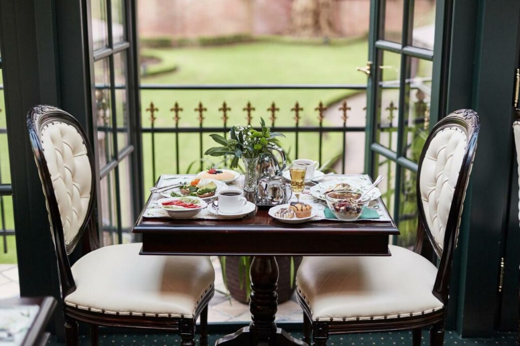 Mesa de café da manhã do Hotel Villa Achenbach com duas cadeiras em cada lado da mesa e café, frutas e pães em cima da mesa.