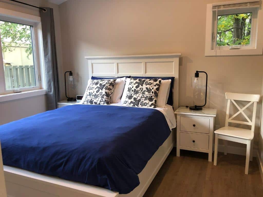 Quarto do Mountain View Bed & Breakfast com uma cama de casal, de cada lado da cama tem uma mesinha branca com um abajur e ao lado da mesinha direita tem uma cadeira branca. O chão é de madeira e tem uma janela pequena no canto direito e outra janela maior na parede esquerda ao lado da cama, ilustrando post Hotéis em Banff.