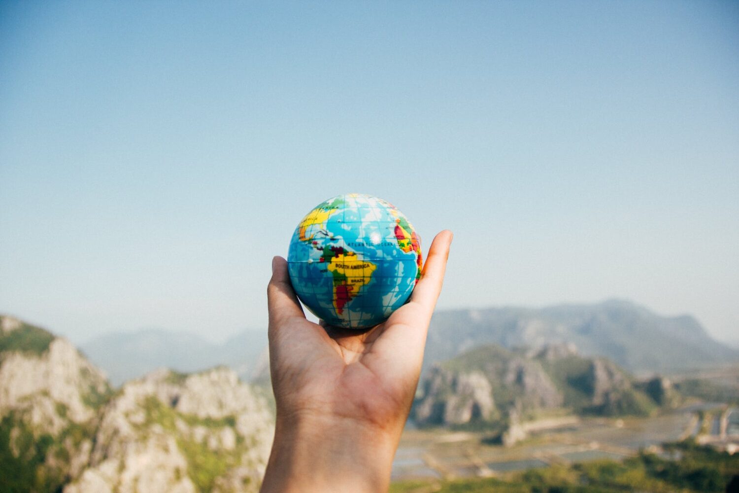 Uma mão segurando um pequeno globo terrestre no ar, para representar seguro viagem internacional