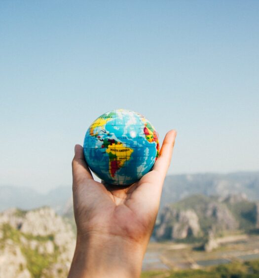 Uma mão segurando um pequeno globo terrestre no ar, para representar seguro viagem internacional