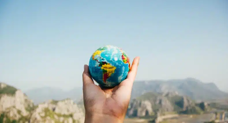 Uma mão segurando um pequeno globo terrestre no ar, para representar seguro viagem internacional