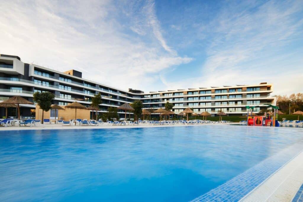 Piscina ao ar livre do  RR Alvor Baía Resort a frente do outro lado da piscina cadeiras e o hotel.