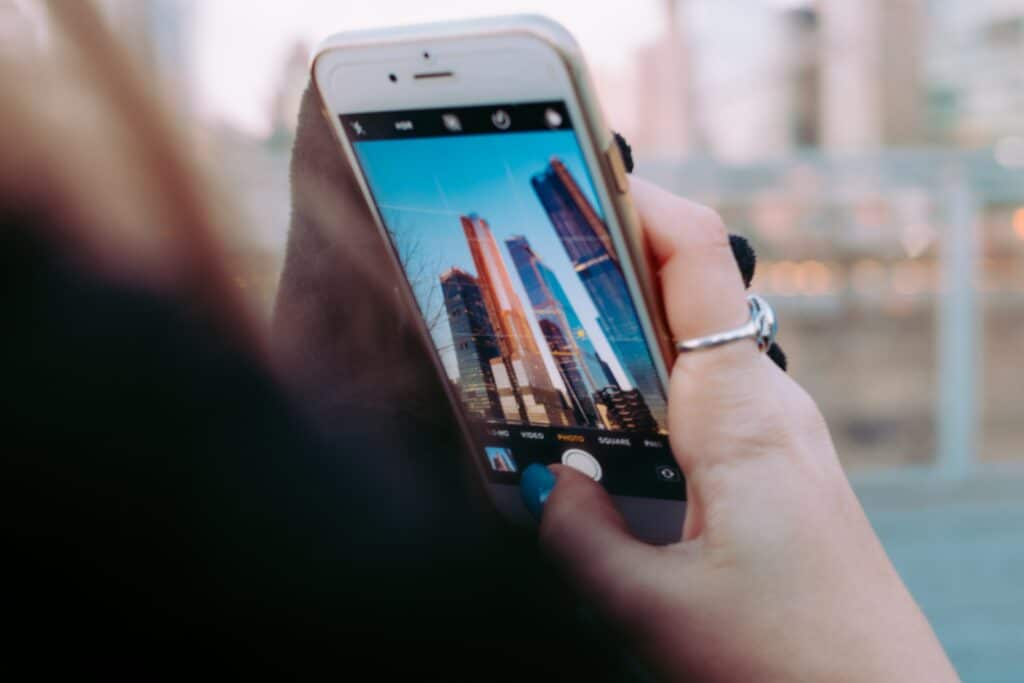 mulher branca fotografando os prédios de Nova York. Ela usa um anel de prata no dedo indicado direito e está com as unhas pintadas de azul.