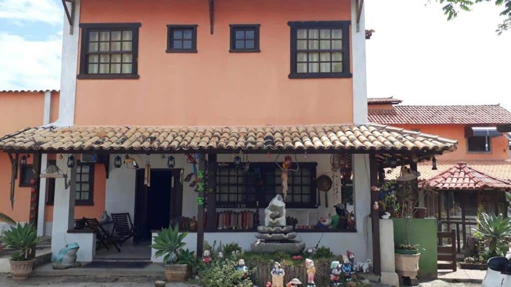 Fachada da Pousada Casa D` Guio com dois andares na cor laranja, quatro janelas no segundo andar e uma no primeiro. Além disso, tem vários objetos de decoração na frente e algumas plantas também, ilustrando post Pousadas em Rio das Ostras.